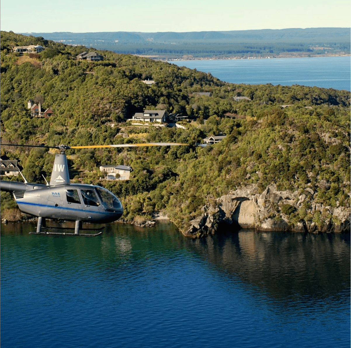 Helicopter skimming coastal inlet near rugged shoreline homes