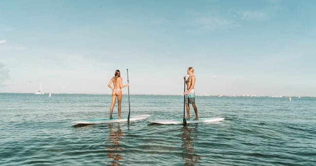 Two stand-up paddleboarders on calm open ocean at sunrise