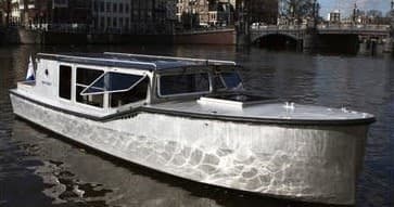 Aluminum tour boat moored on Amsterdam canal reflecting cityscape