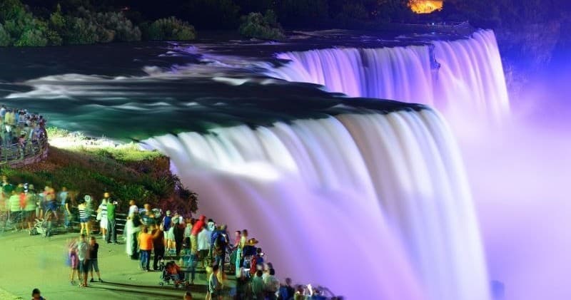 Crowd viewing illuminated Niagara Falls at night from riverside lookout