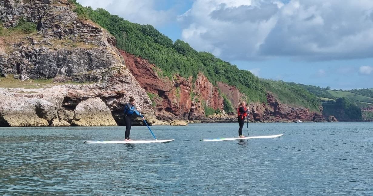 Paddleboarders exploring rugged coastal cliffs on sea