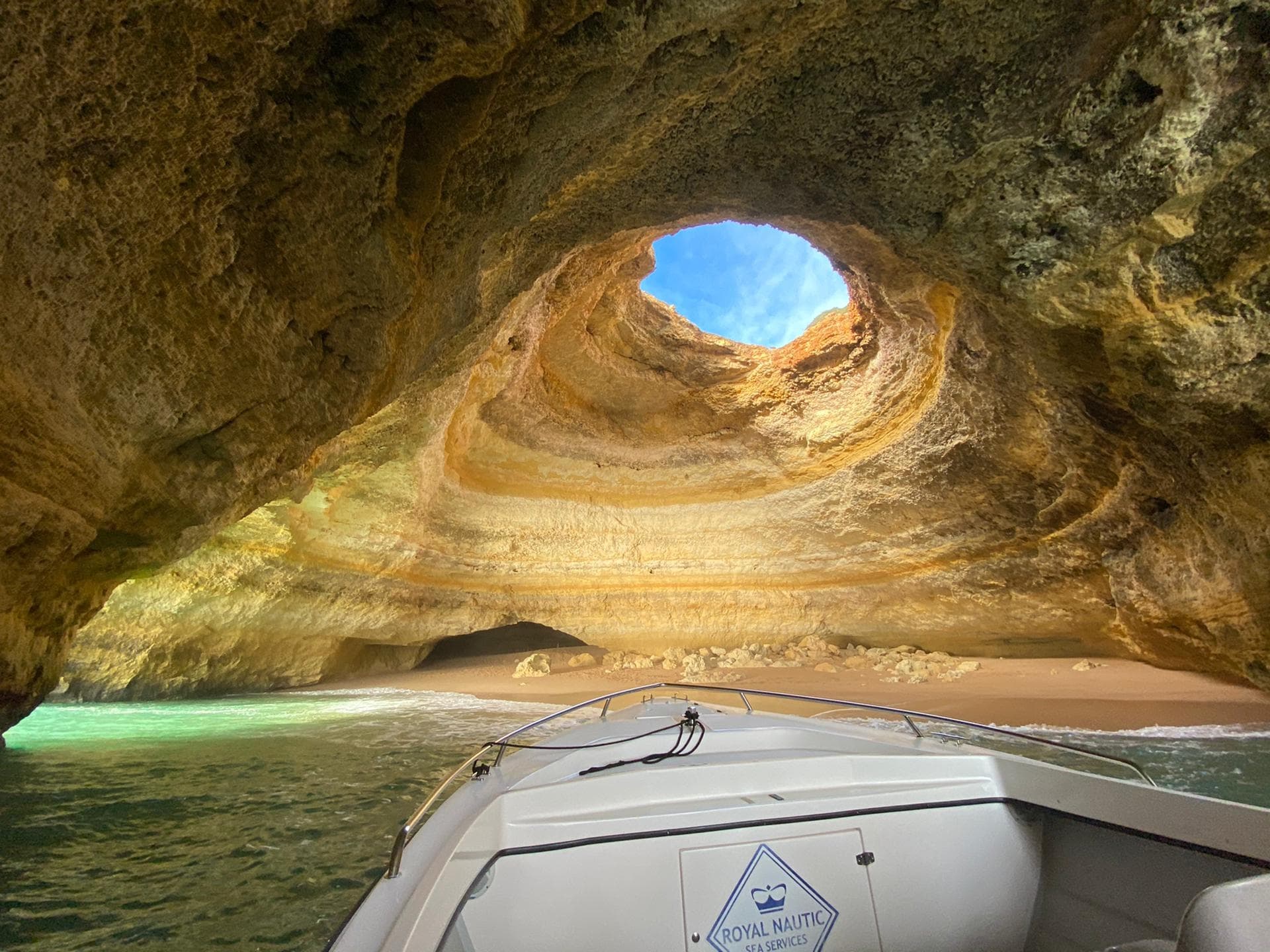 Boat approaching dramatic sea cave skylight and sandy cavern
