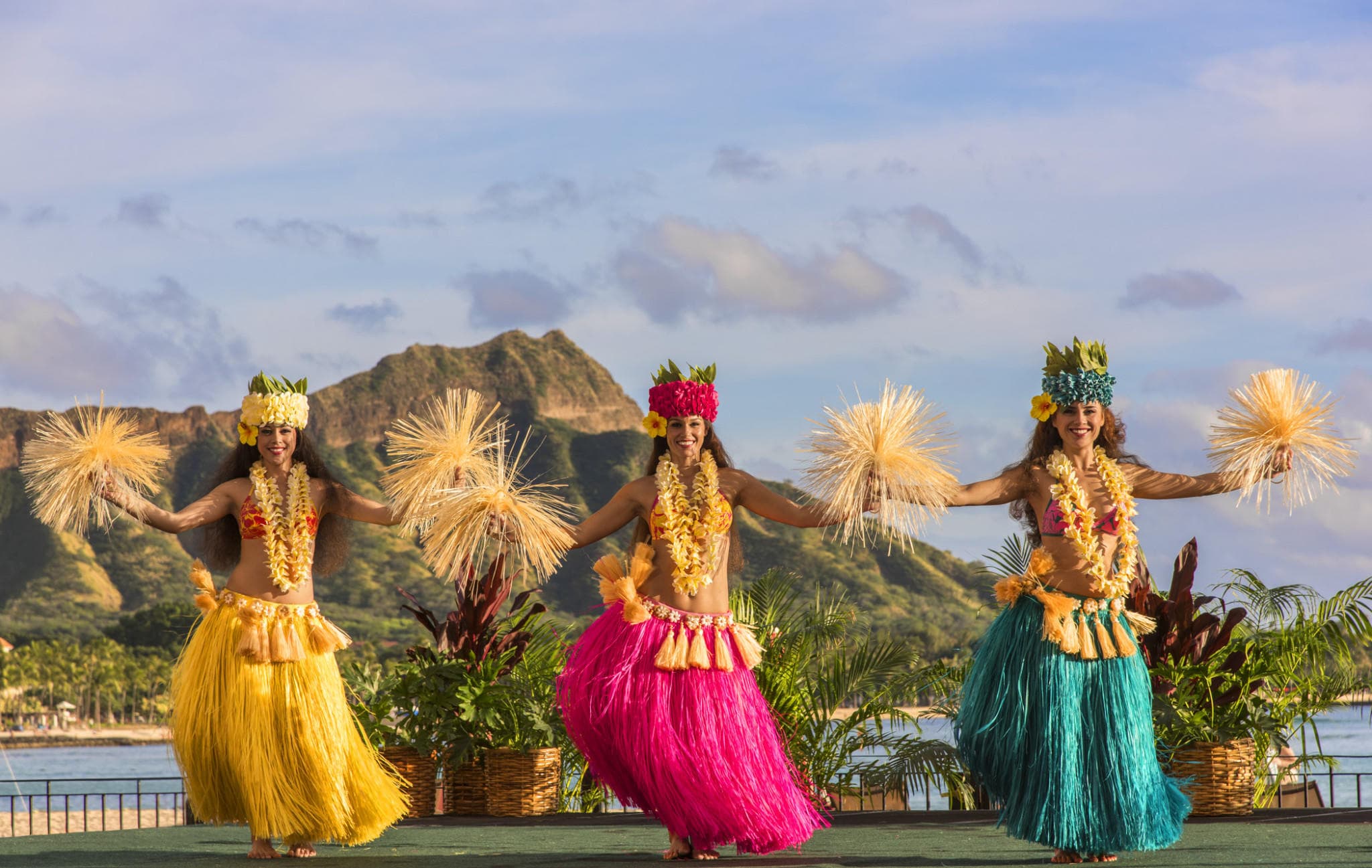Hula dancers performing on Waikiki beachfront stage with mountains