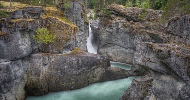 Waterfall carving rocky canyon, turquoise river in forest