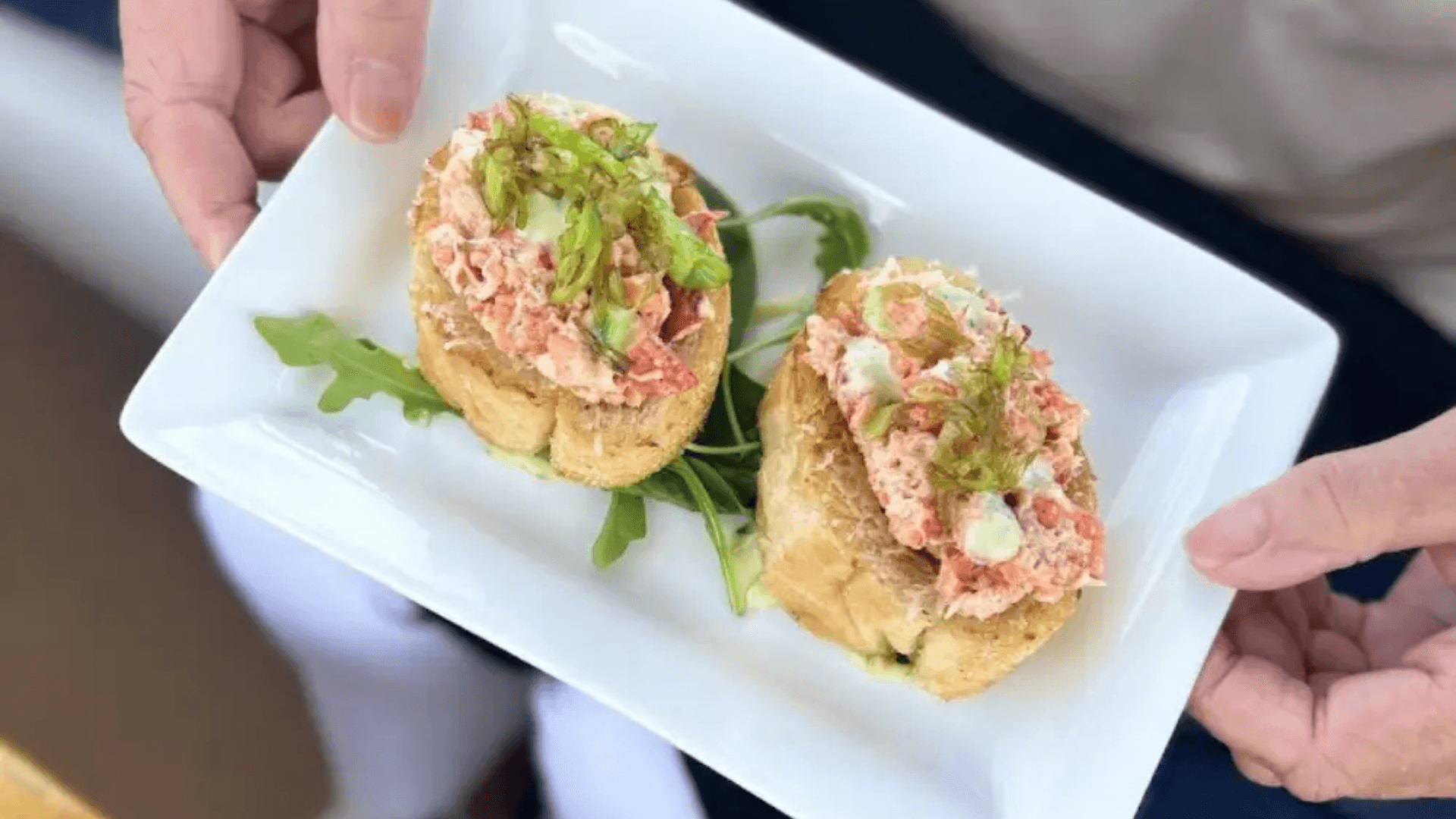Lobster rolls plated on boat with arugula garnish seaside bite