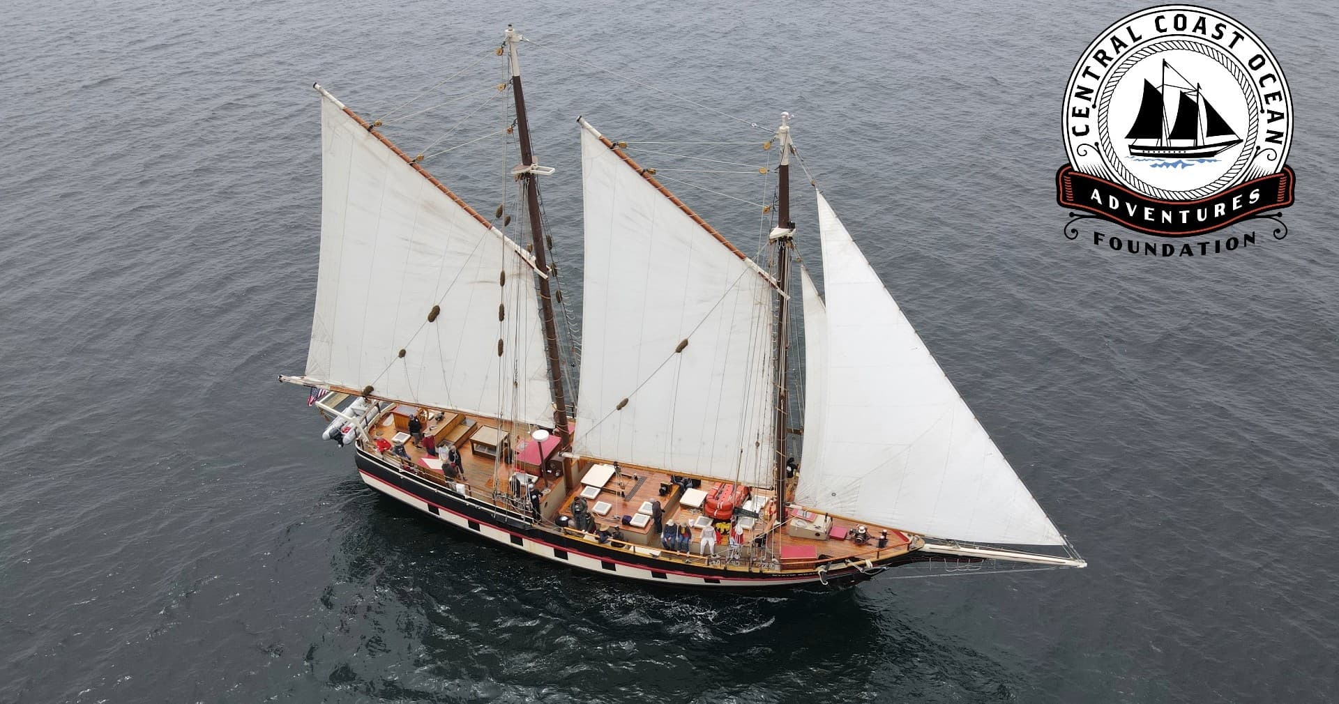 Aerial schooner cruise on calm grey ocean with sails unfurled