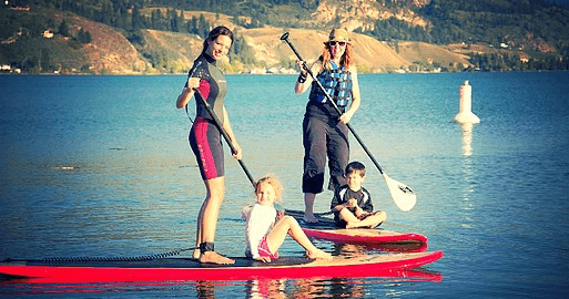 Family standup paddleboarding together on scenic lake shore