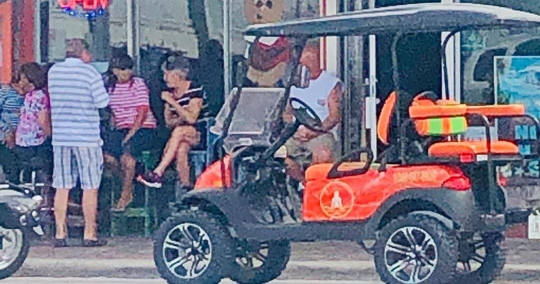 Orange beachside golf cart near crowded boardwalk and shops