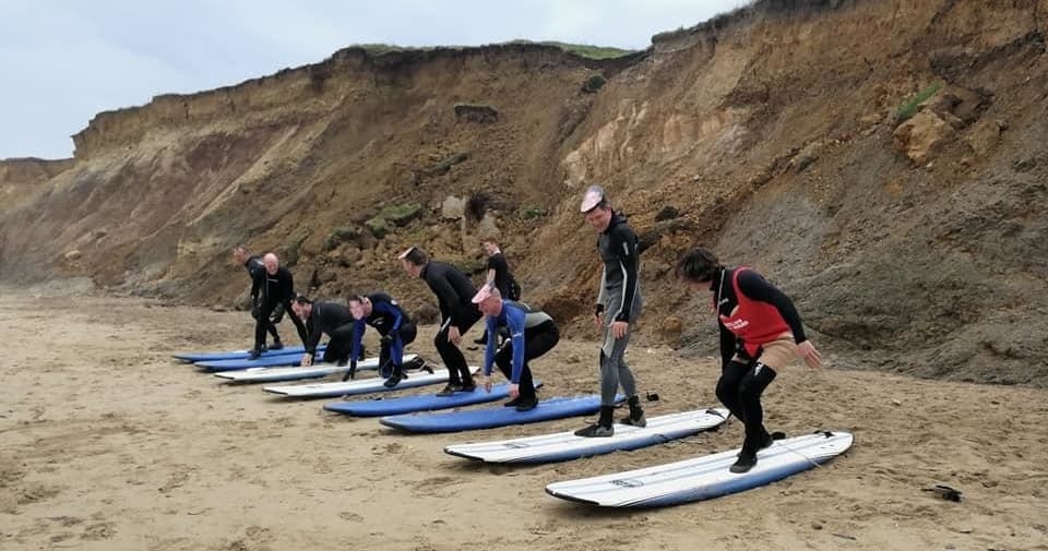 Group surf lesson on sandy beach below dramatic cliffs