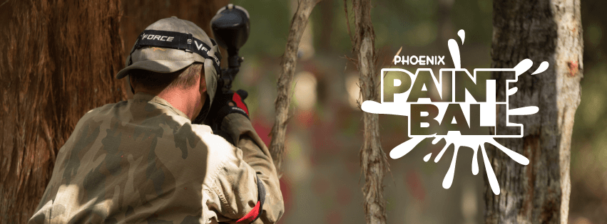 Player in camo taking aim behind tree in woodland paintball field