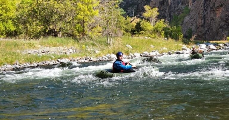 Packrafter navigating mild whitewater on forested Colorado river