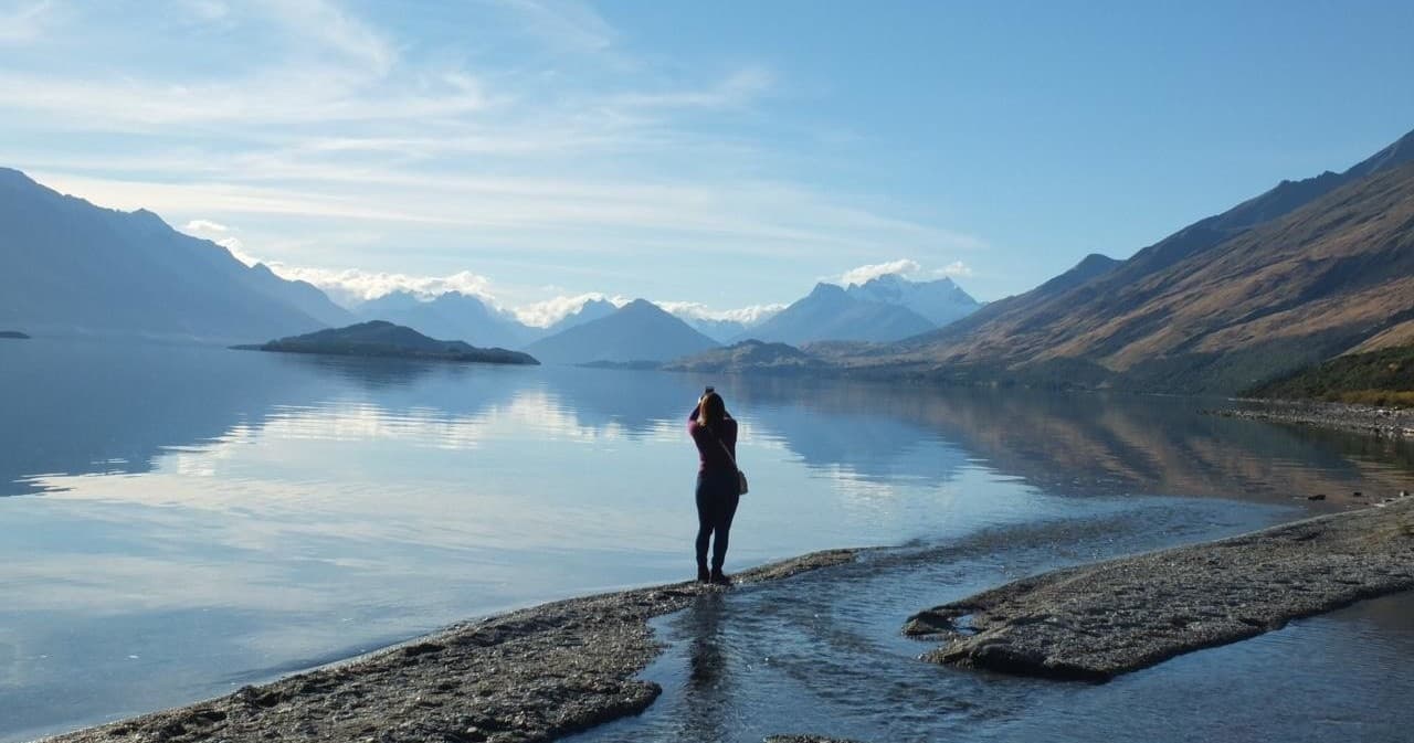 Solo hiker standing on reflective alpine lake shore in New Zealand