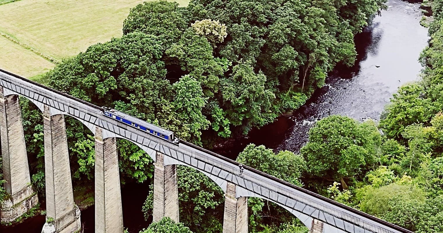 Train crossing riverside viaduct through lush forest for scenic rides