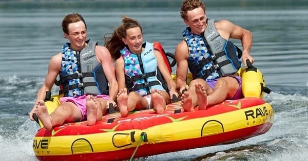 Three people tubing behind boat on Minnesota lake, summer fun