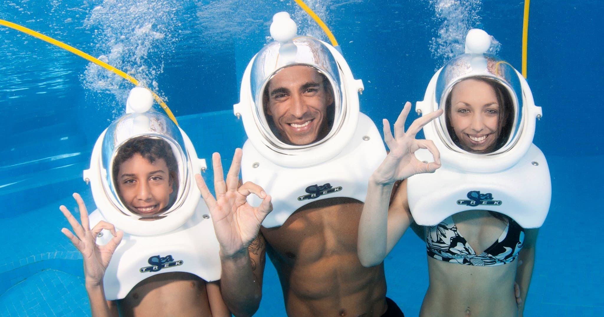 Underwater sea-walkers in helmets smiling amid blue ocean