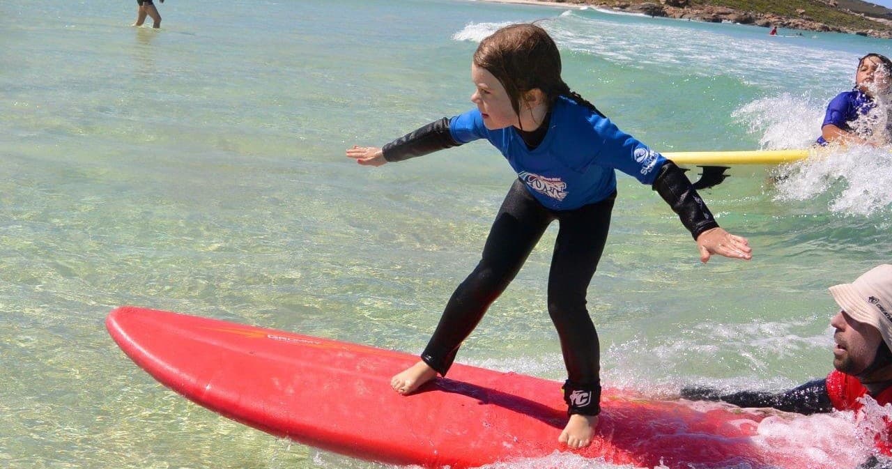 Child surfing on red board in shallow waves at Margaret River