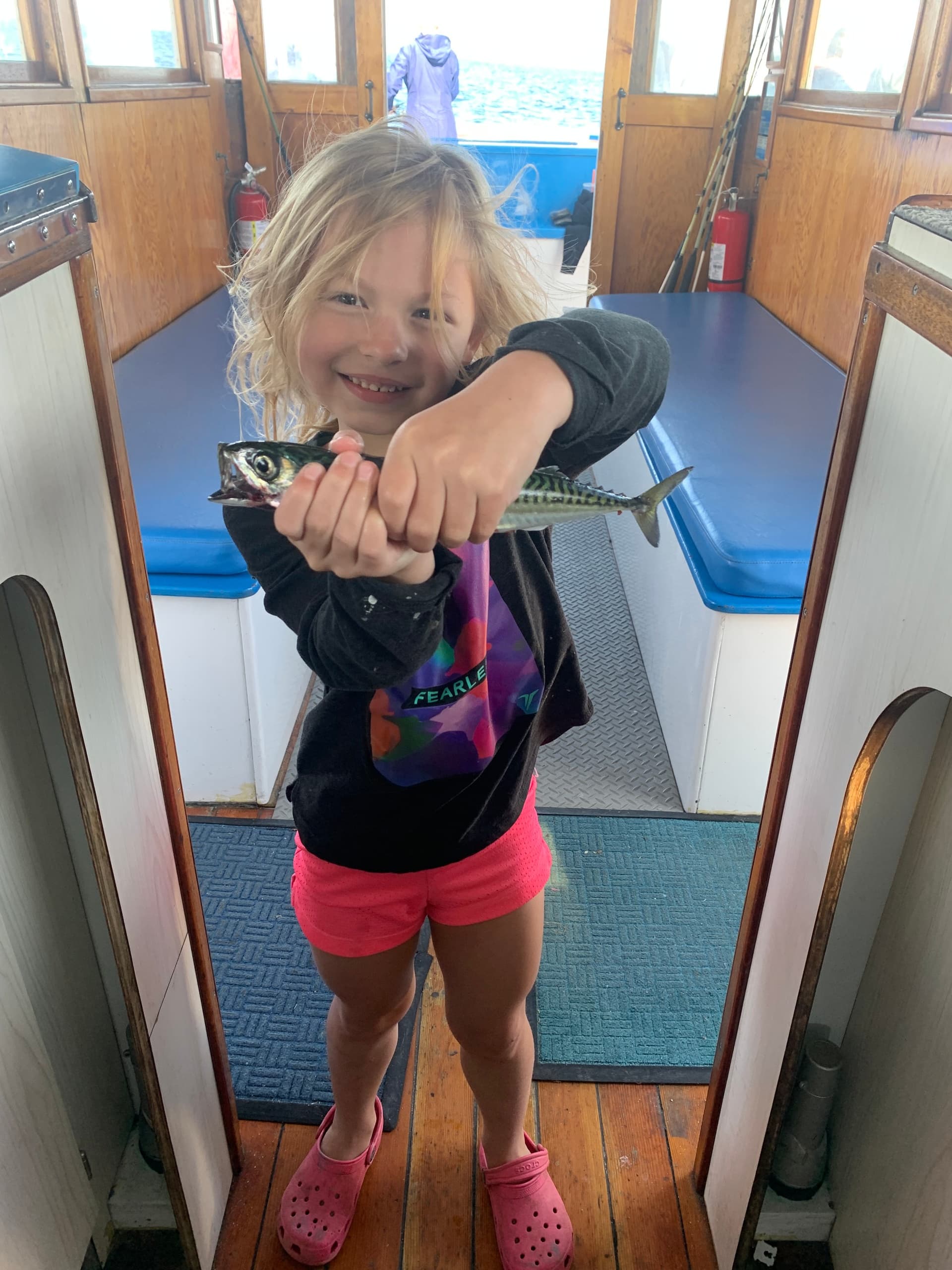 Child angler holding small mackerel in cabin on family fishing trip