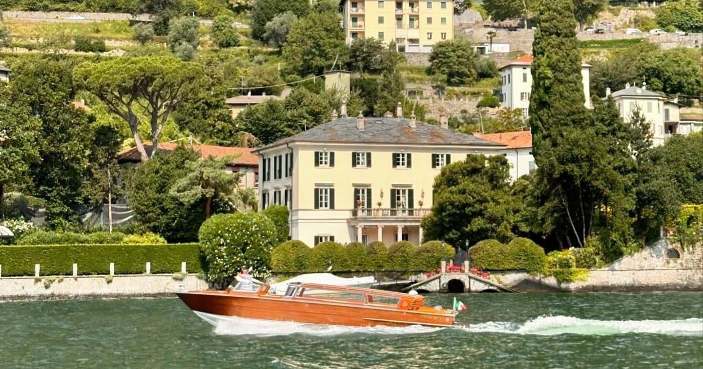 Classic wooden speedboat cruising past villa on emerald lake