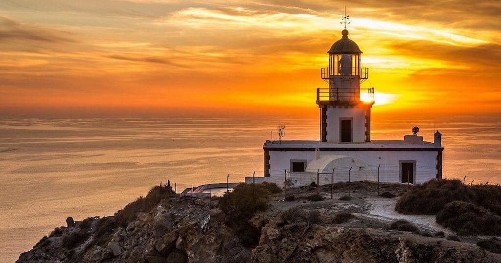 Coastal lighthouse at sunset on rocky headland by the sea