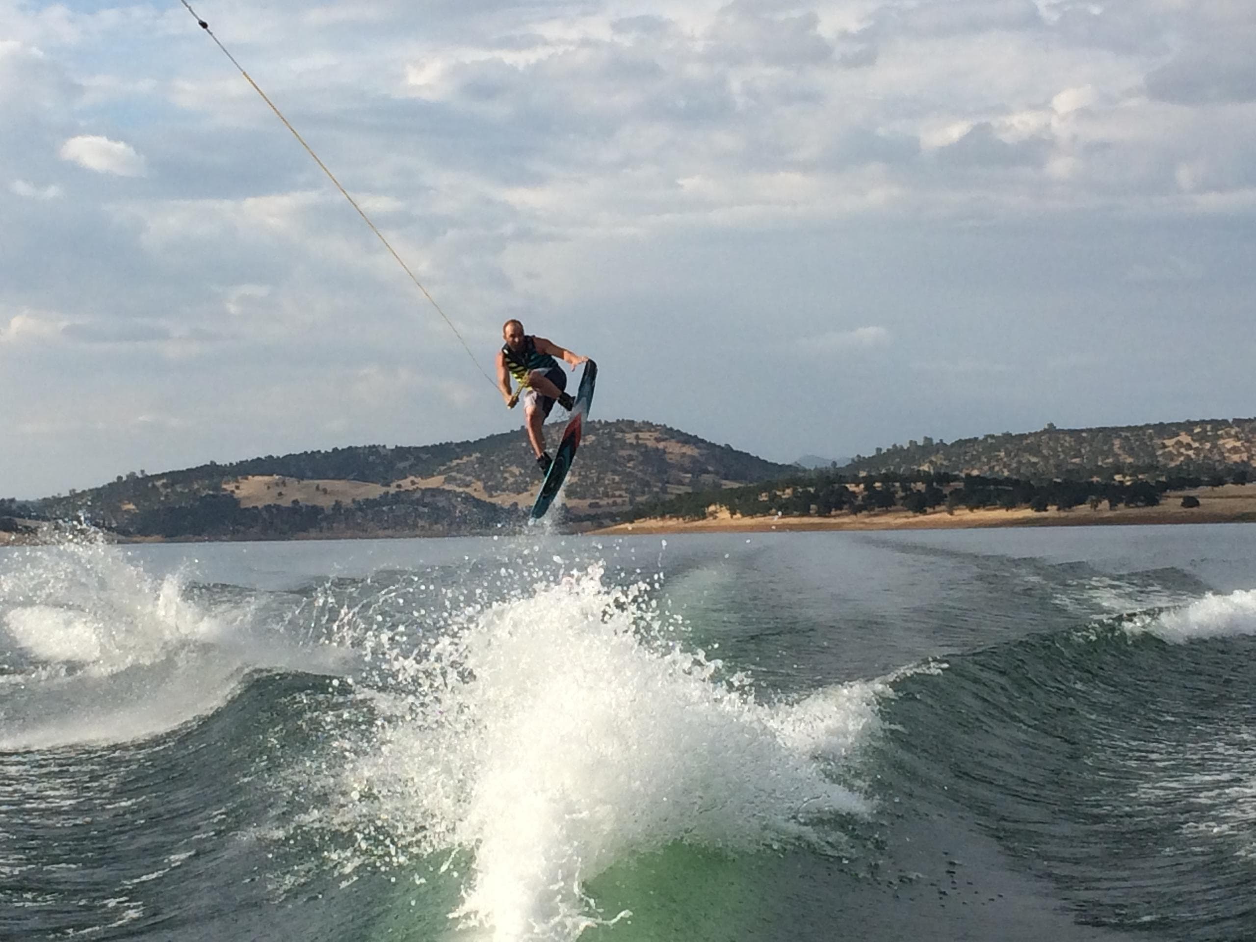 Wakeboarder jumping over wake with mountainous lake backdrop
