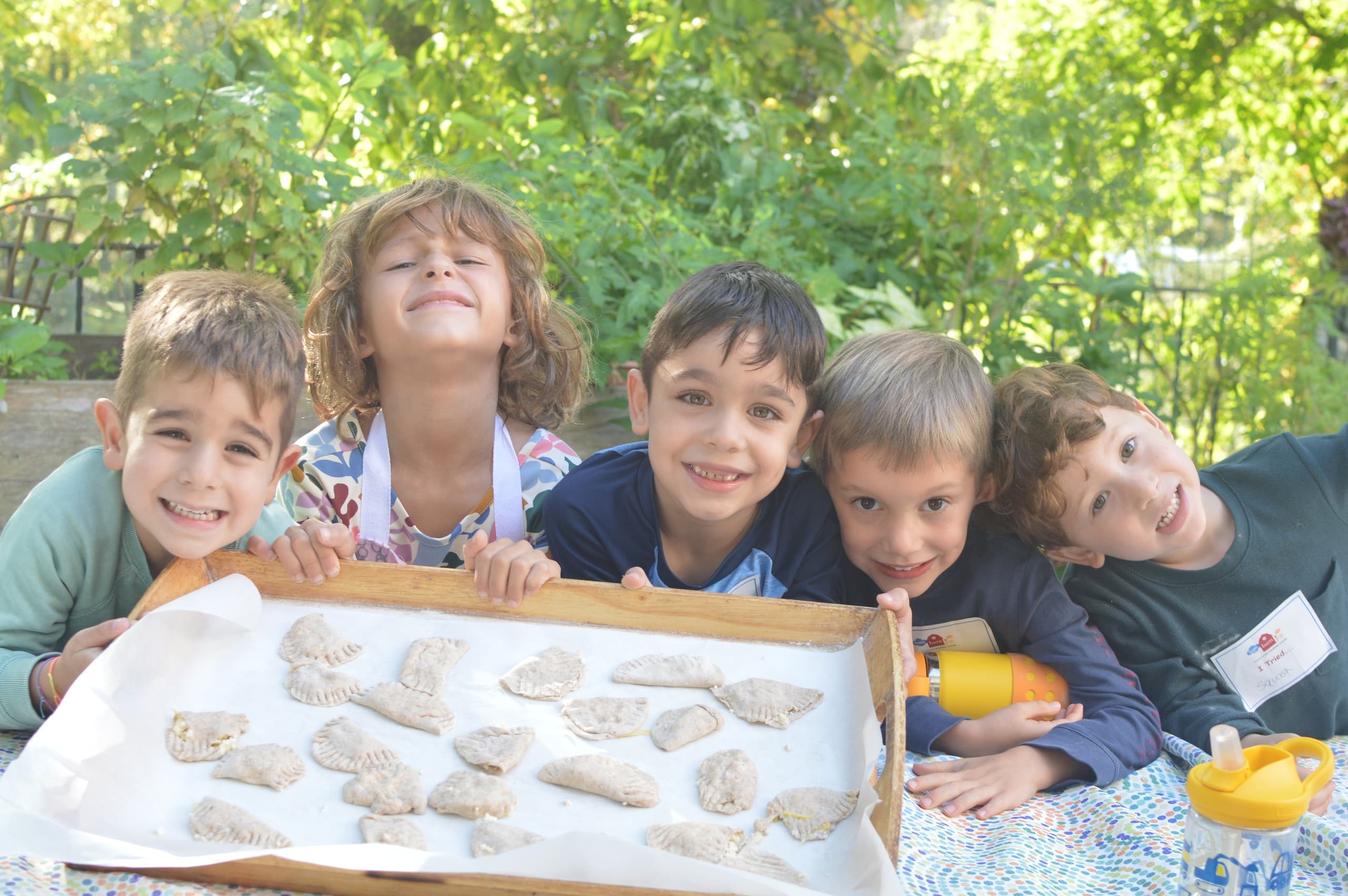 Children displaying craft tray outdoors at a nature table