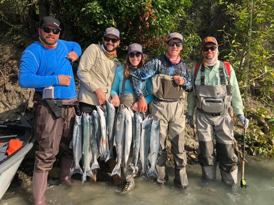 Guided fishing group holding multiple salmon on Alaska riverbank
