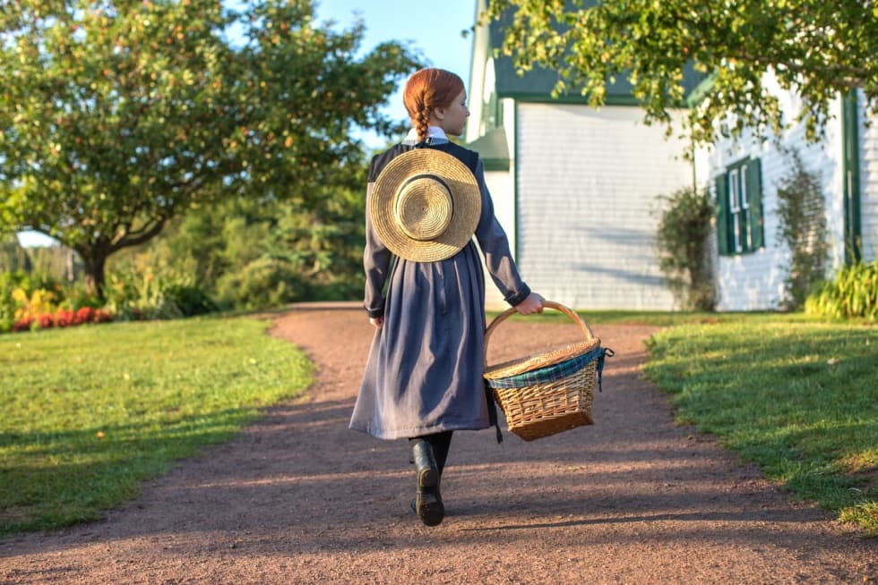 Woman walking on rural path with picnic basket near farmhouse