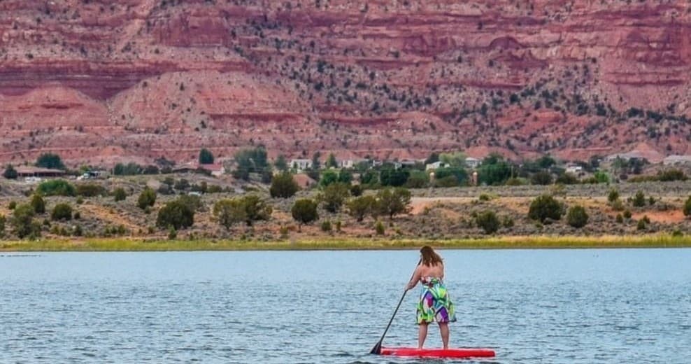 Stand-up paddleboarding on calm lake with red cliffs backdrop