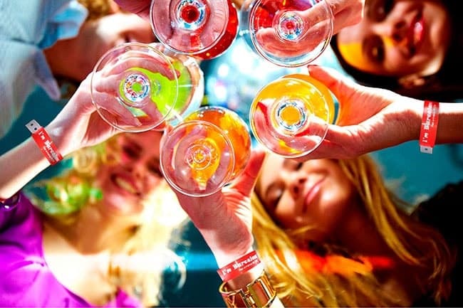 Friends toasting colorful cocktails at lively indoor party