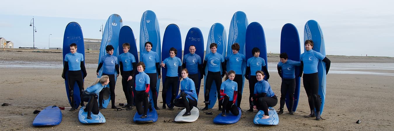 Group of surfers with blue boards lined up on sandy beach