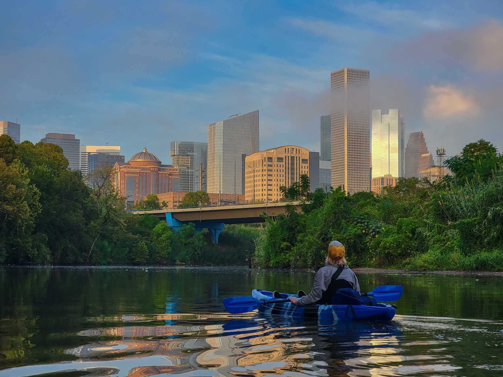 Kayaker floating toward city skyline on reflective river