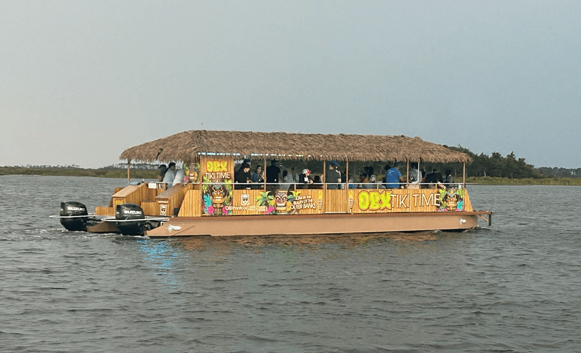 Tiki-style pontoon boat cruising coastal inlet with passengers