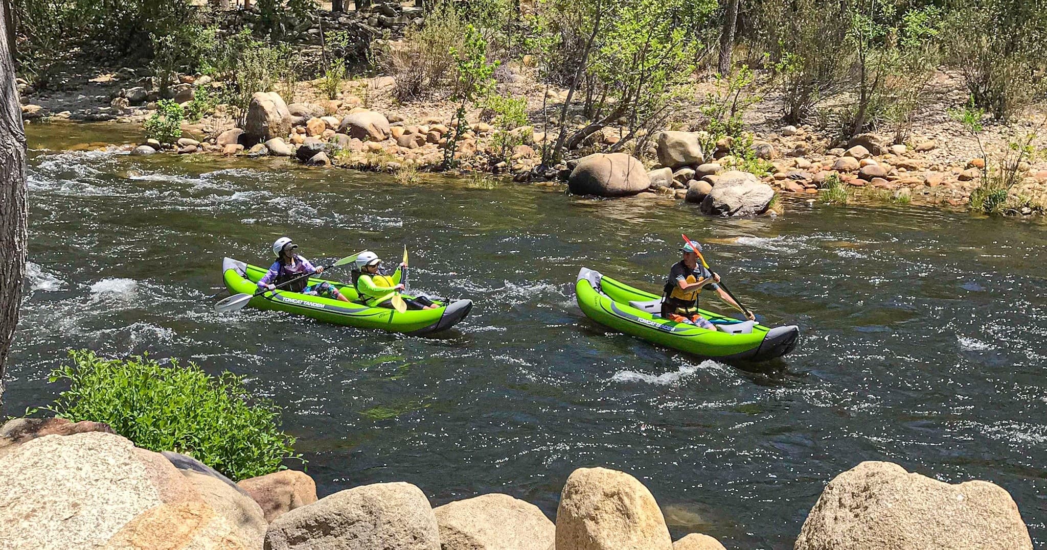 Two green kayaks paddling past rocky river shoreline, scenic float