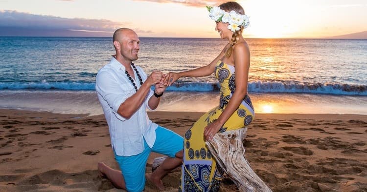 Couple beach proposal at sunset on Maui shoreline with leis
