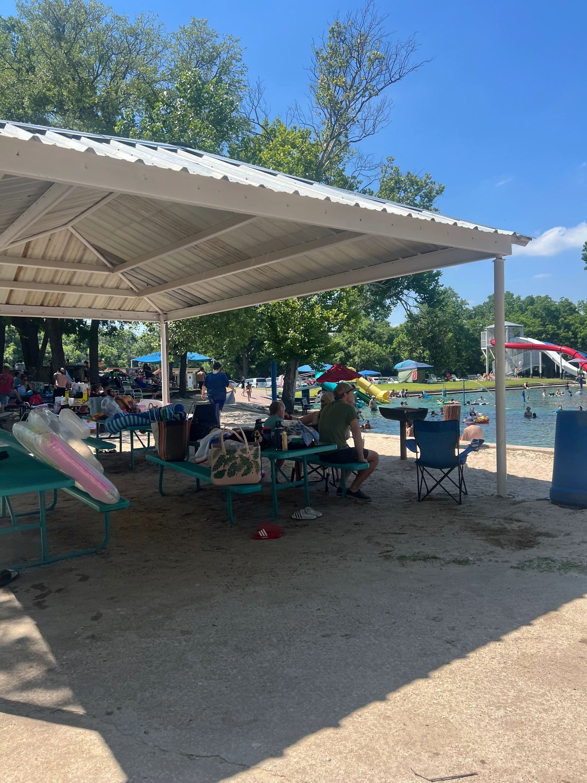 Crowded picnic shelter near lake with swimmers and chairs