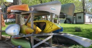 Multiple kayaks and canoes stored on rack near riverside cottage