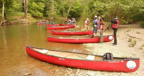 Row of red canoes on sandy riverbank, group preparing to launch