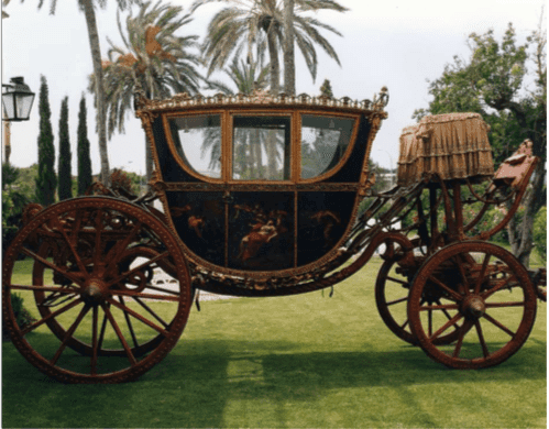 Antique horse-drawn carriage displayed on manicured lawn under palms