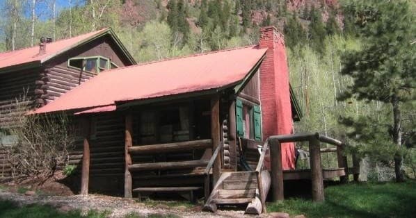 Rustic log cabin with red roof in forested mountain meadow