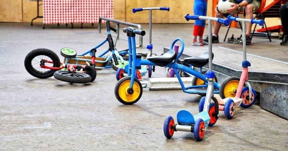 Children's balance bikes and scooters lined up at indoor activity area