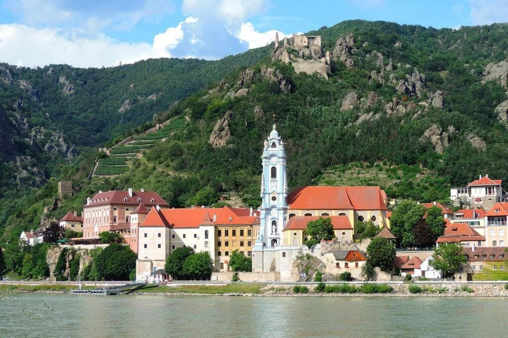 Riverside town and church with mountain backdrop, scenic stroll