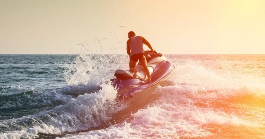 Jet ski silhouette jumping waves at golden sunset on ocean