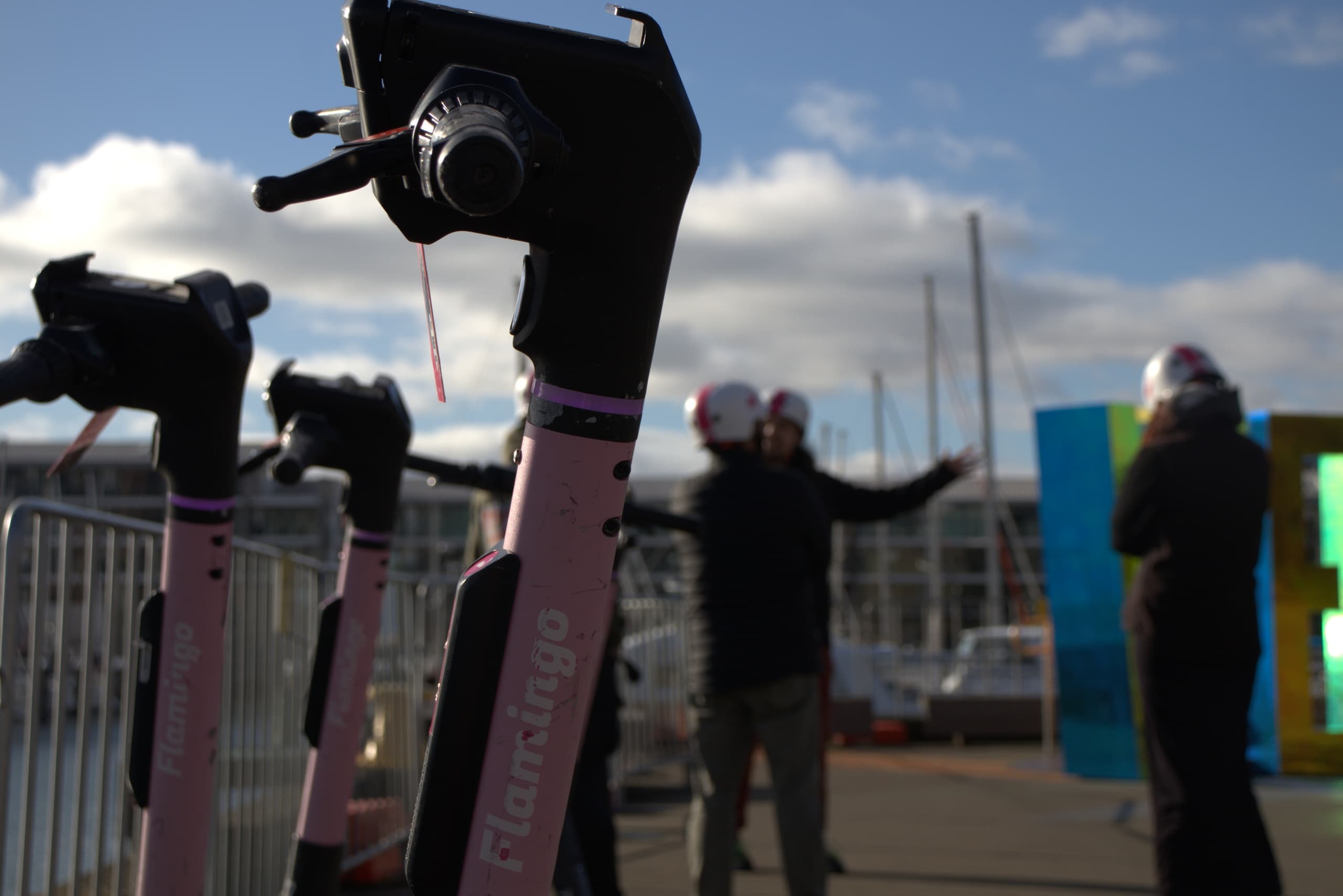 Dockside electric scooters and riders by marina on sunny day