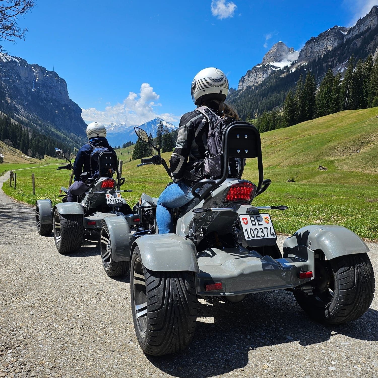 Three-wheelers cruising valley road with alpine peaks in background