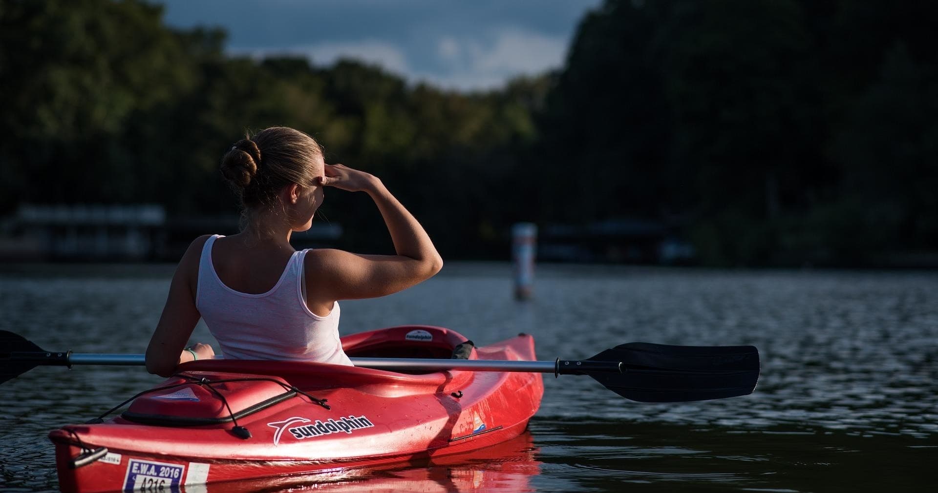 Solo kayaker paddling at dusk on calm river with tree-lined shore