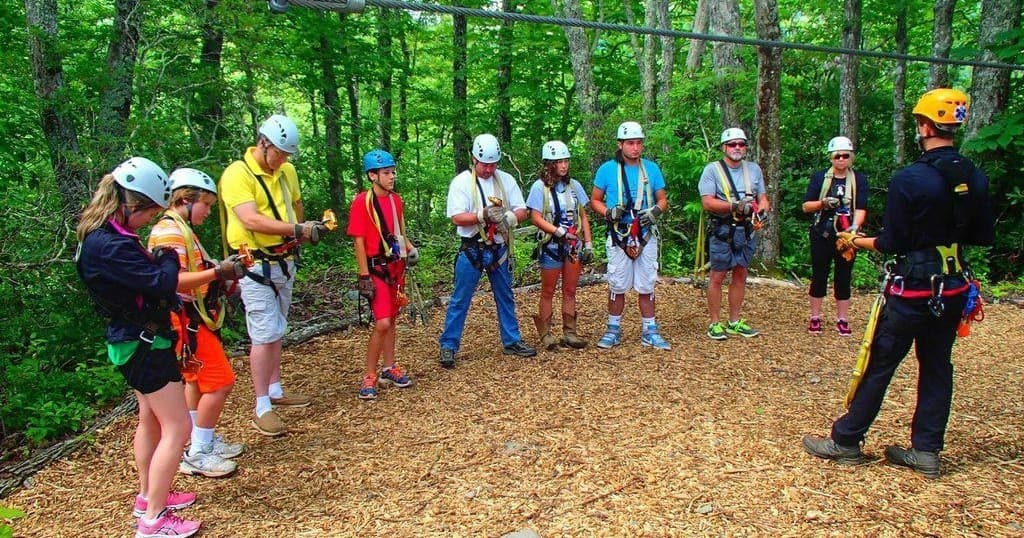 Guided zipline safety briefing with group in wooded canopy setting