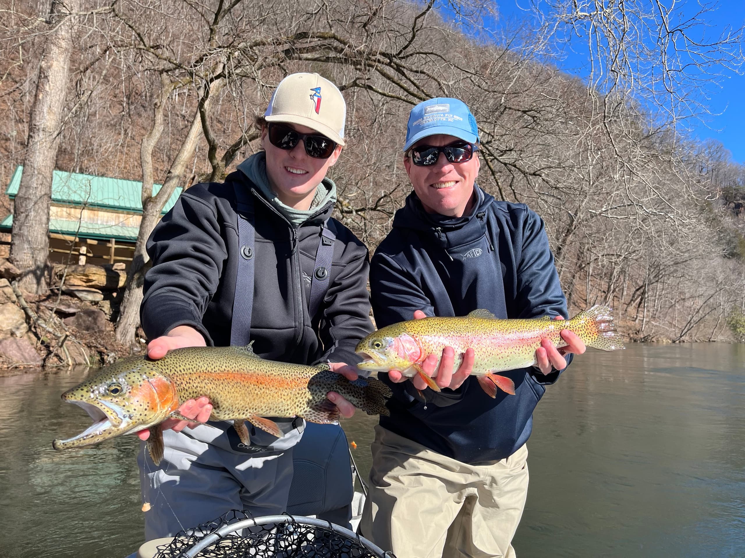 Two fishermen presenting colorful rainbow trout on riverbank guide