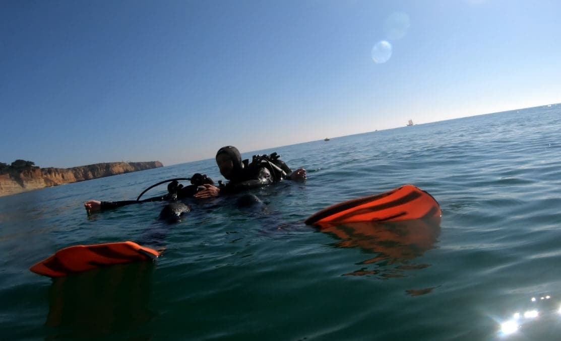 Scuba divers at sea surface with orange safety buoys and sun