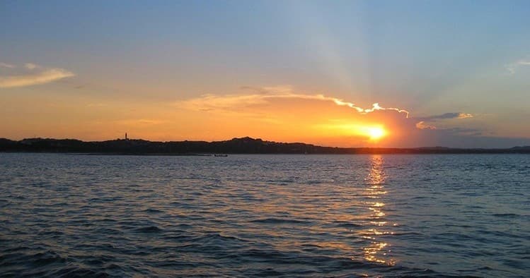Sunset over open lake with distant shoreline, serene boating
