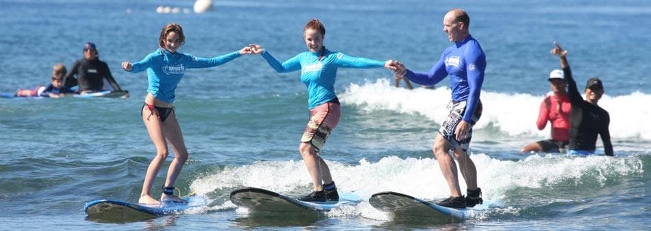 Three surfers riding a small wave together off Maui shore